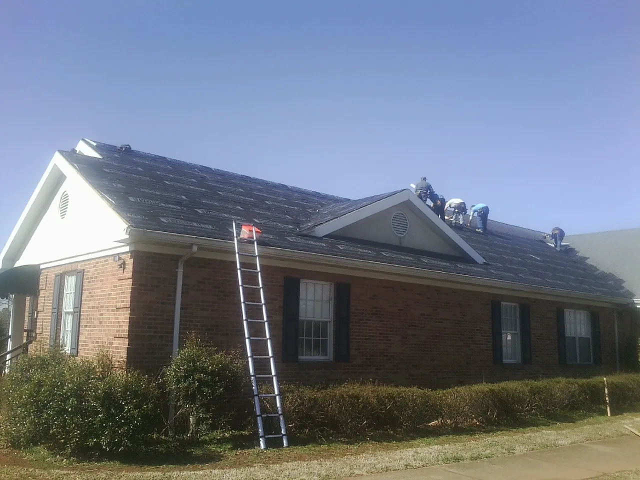 Crew tearing shingles off a brick ranch roof with a ladder set — Emergency Roof Repair work by our crew in Lagro