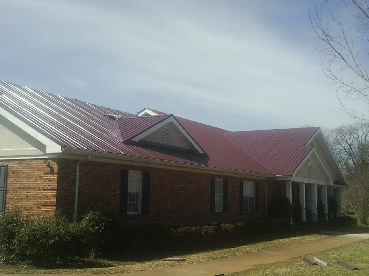 Red metal roof with gabled entries on a long brick building, from a Hail Damage Roof Repair job in Lagro