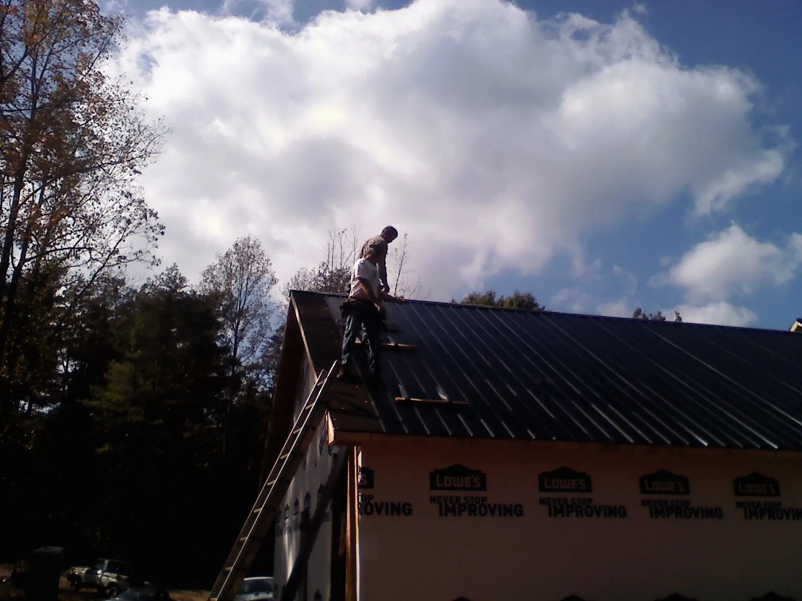 Roofer fastening dark metal panels high against a cloudy sky, from a Roof Inspection job in Lagro