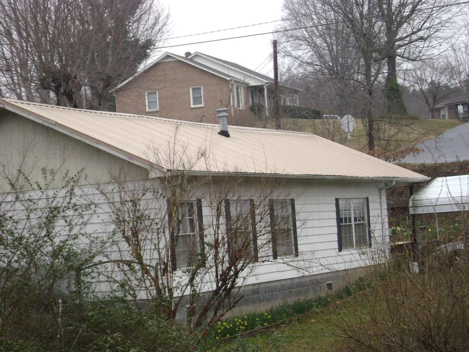 Tan metal roof on a white sided house set into a hillside — Commercial Roofing by Roofing Brothers in Lagro
