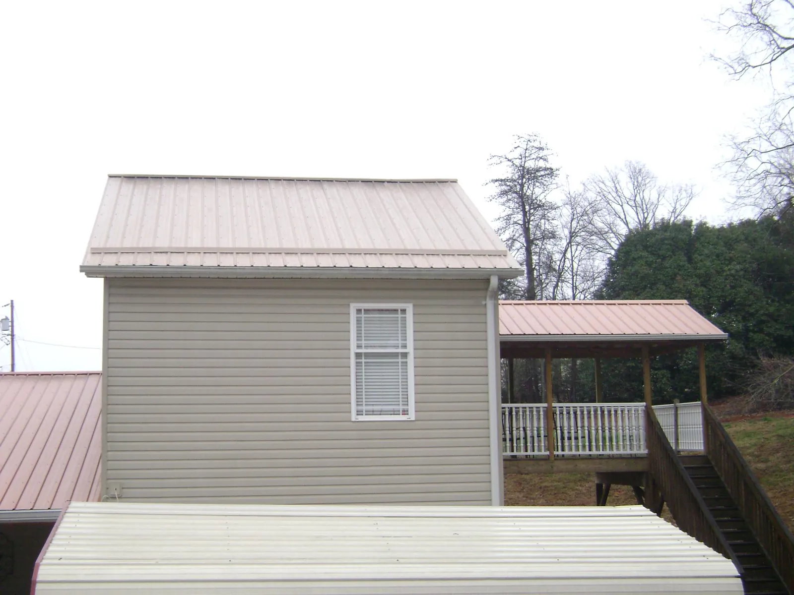 Tan metal roofs on a two story addition and attached porch, from a Roof Replacement job in Lagro